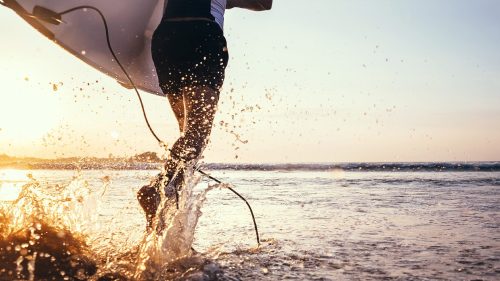 A person running into the sea with a surfboard