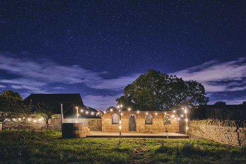The outside of Orchard Snug in Somerset in the evening with hot tub and festoon lights